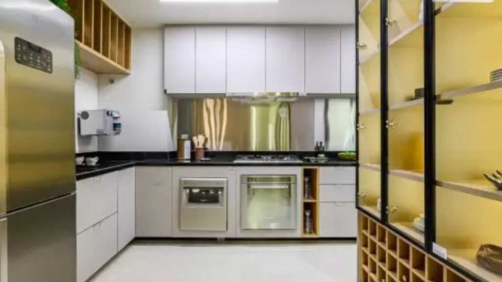 Cozinha moderna em estilo corredor de um apartamento 2 quartos Noroeste, com armários brancos, bancada de granito preto, eletrodomésticos em inox e adega de madeira.
