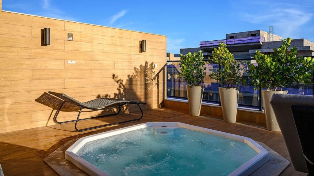 Deck de madeira com hidromassagem aquecida na cobertura, espreguiçadeira e paisagismo em vasos em um Apartamento 4 Quartos Noroeste - Residencial Singular.