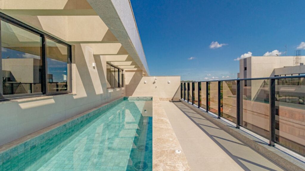 Piscina com raia na cobertura coletiva de um edifício residencial, apresentando deck em pedra, guarda-corpo de vidro e vista livre, ideal para quem busca um apartamento 2 quartos Noroeste.