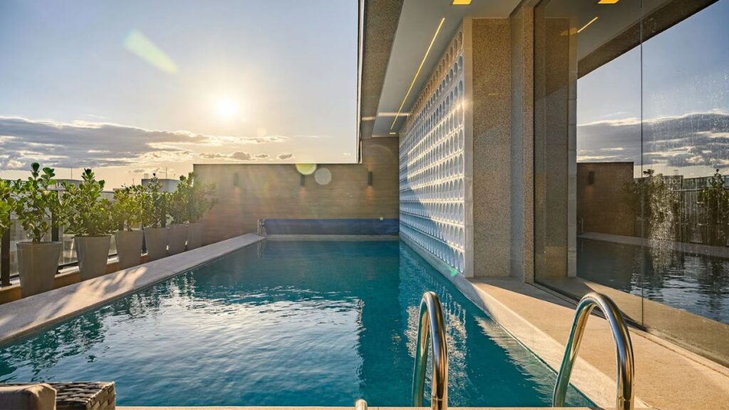 Piscina com raia na cobertura coletiva de um prédio de Apartamento 4 Quartos Noroeste - Residencial Singular, com deck, painel vazado e vista livre no pôr do sol.