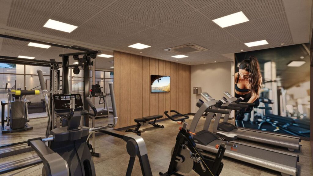 Academia moderna do Residencial Unité em Águas Claras, equipada com esteiras, bicicletas ergométricas, aparelhos de musculação e painéis amadeirados com TV.