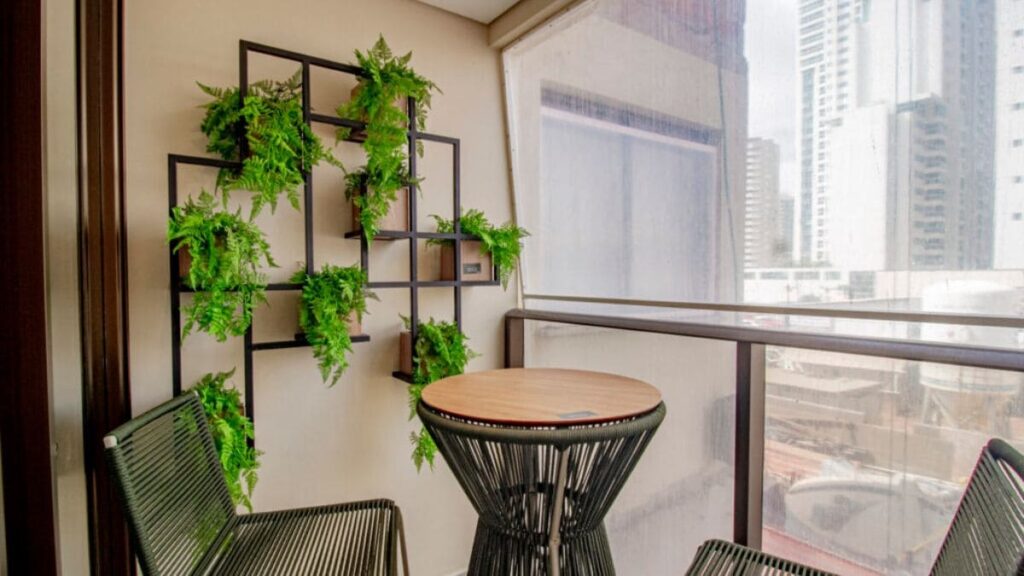 Varanda decorada do Residencial Unité em Águas Claras, com jardim vertical em estrutura metálica preta, mesa bistrô redonda e cadeiras de corda náutica verde.