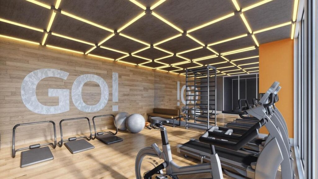 Perspectiva eletrônica da academia moderna do condomínio Portal do Parque II. A imagem mostra um espaço com piso de madeira, equipamentos de musculação e cardio de alta tecnologia, incluindo esteiras e bicicleta ergométrica. A parede de destaque possui um painel de madeira com a inscrição 