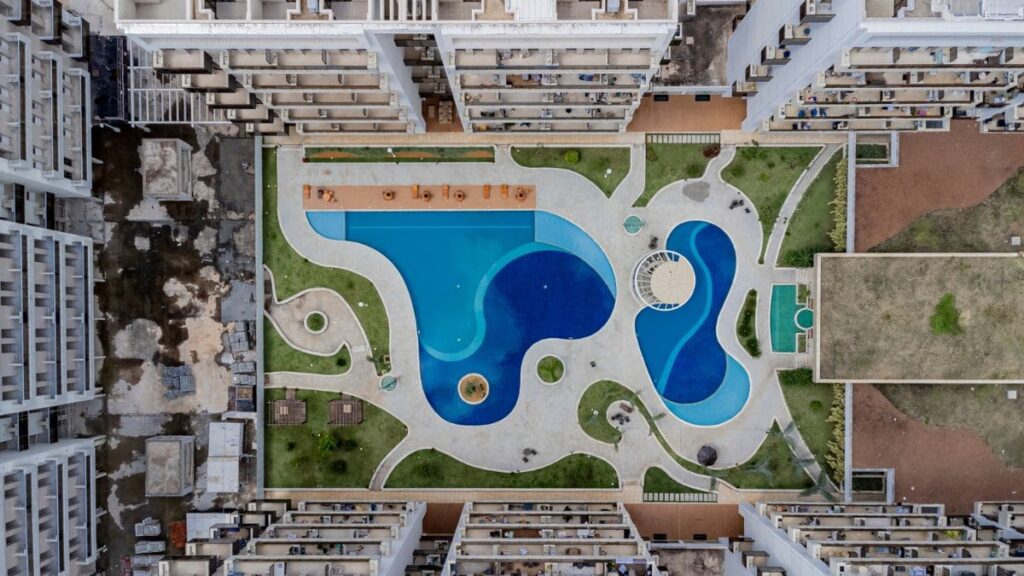 Parque Aquático Exclusivo – Park Sul Vista aérea vertical do parque aquático de um condomínio de Apartamento 2 Quartos Park Sul, exibindo piscinas em formatos orgânicos com diferentes tonalidades de azul, áreas verdes e deck molhado.
