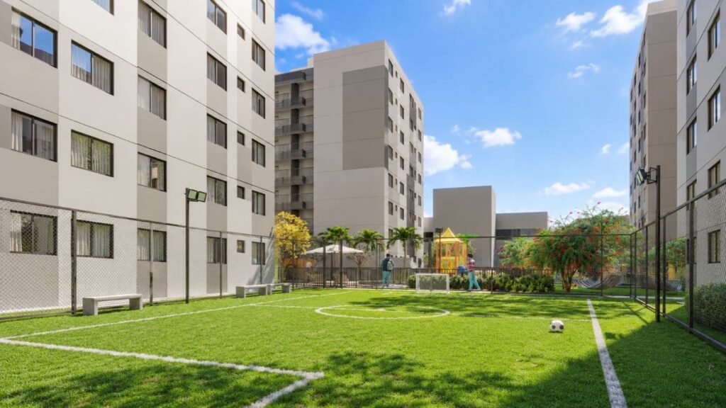 Campo de futebol gramado e cercado por alambrado situado entre os edifícios residenciais do condomínio Nexus Taguatinga